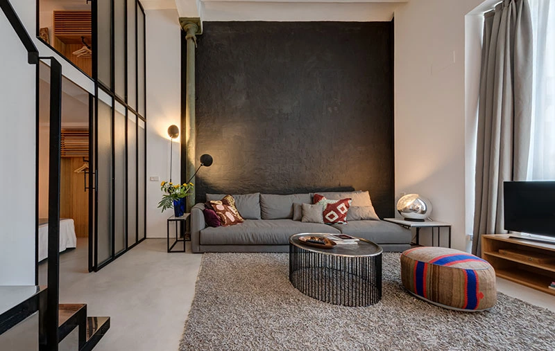 Salotto del loft con soppalco a Siviglia con parete in stucco nero, divano grigio e pouf colorato
