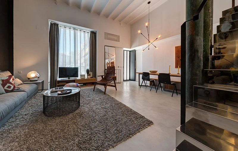 Salotto e zona pranzo del loft con soppalco a Siviglia, con grandi finestre e luce naturale