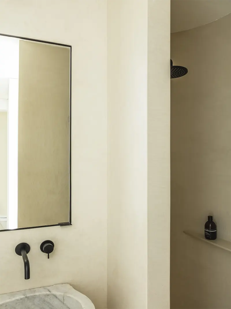 Interno bagno di un mini appartamento con lavandino in marmo e doccia a pioggia.