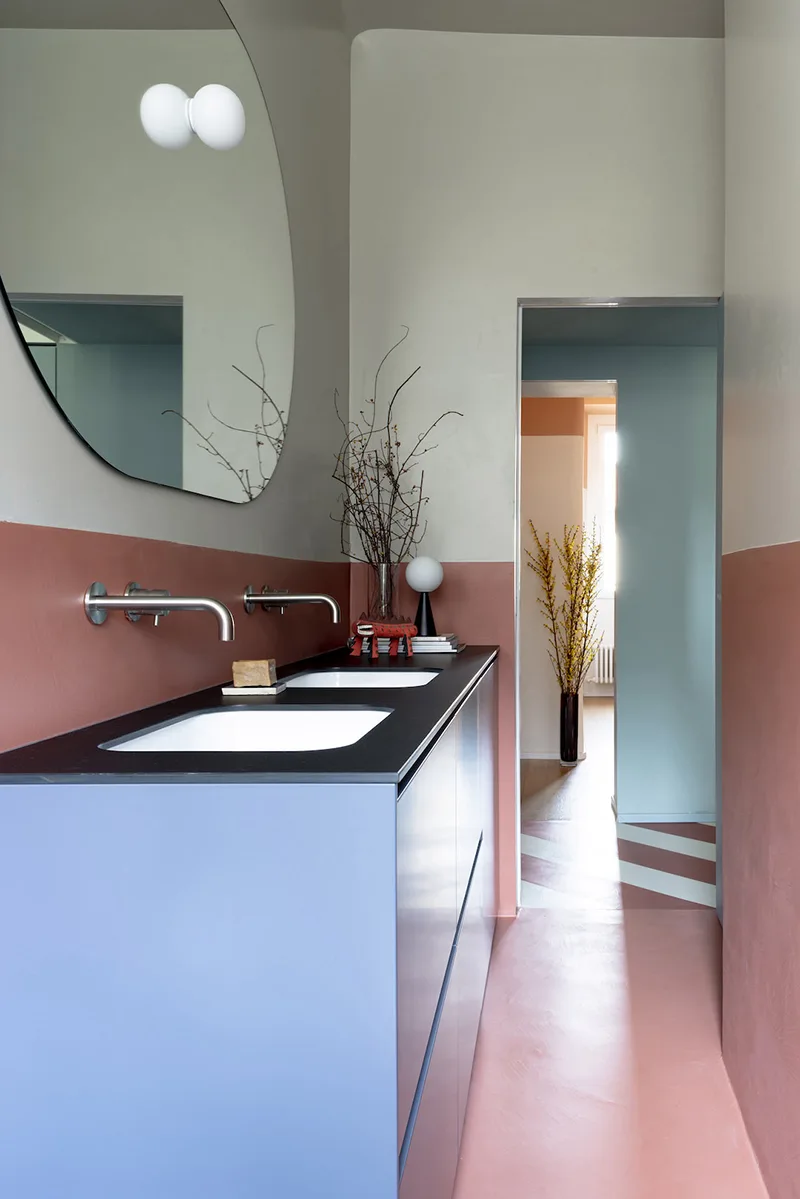 Bagno con doppio lavabo e vista sul corridoio a righe rosse, dettaglio del progetto Atelierzero per rinnovare con il colore