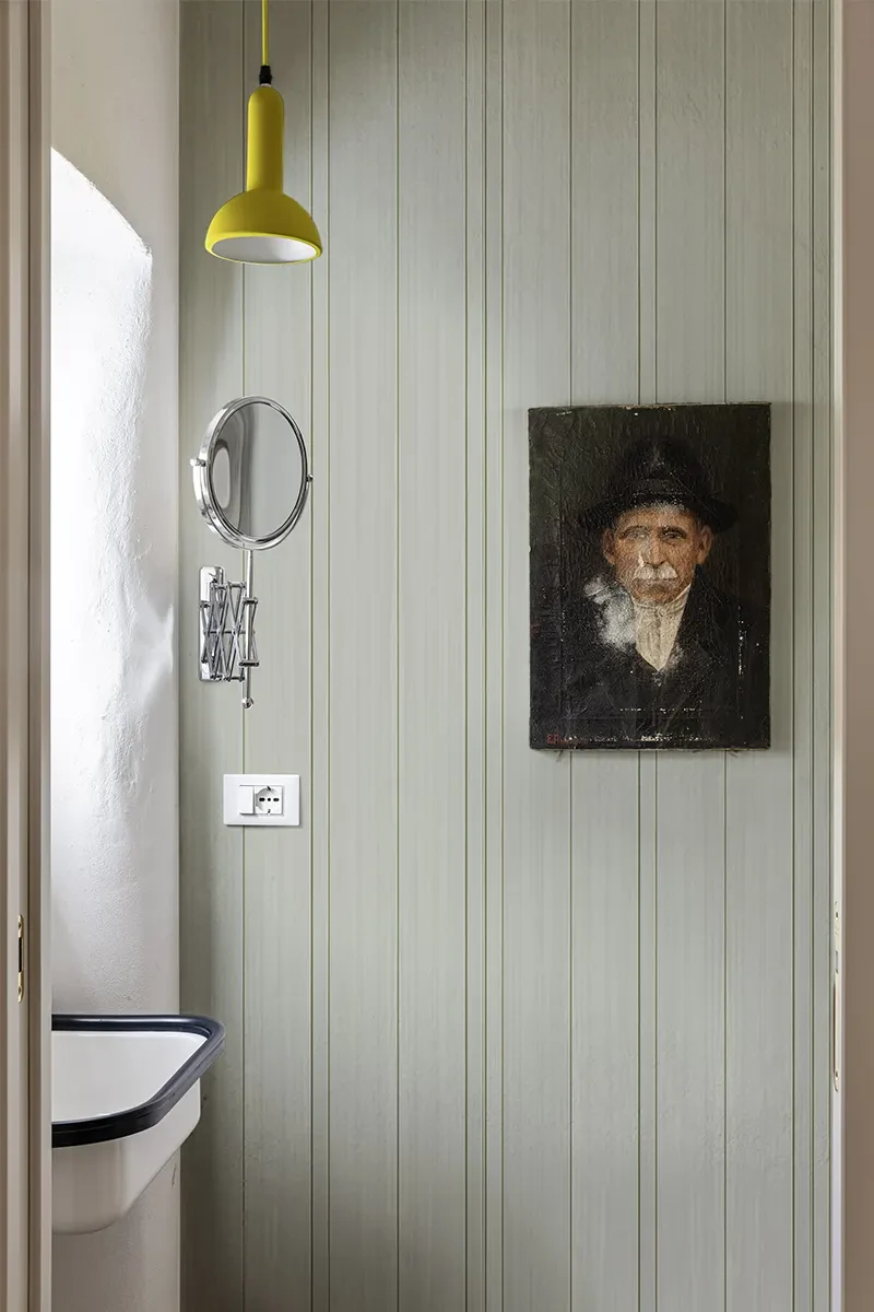 Carta da parati in fibra di vetro modello Wallpleats di SpaghettiWall a righe verticali sottili verde salvia in un bagno piccolo moderno con lavabo compatto.