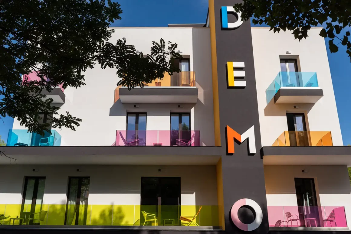 Facciata esterna di Demo Hotel a Rimini con logo colorato e balconi in vetro