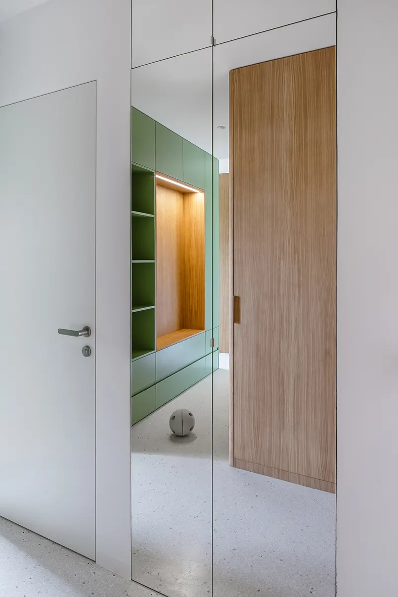 Il cubo verde che riorganizza lo spazio: dentro un piccolo appartamento a Praga 5 Armadio a specchio nell'ingresso che riflette il cubo verde centrale