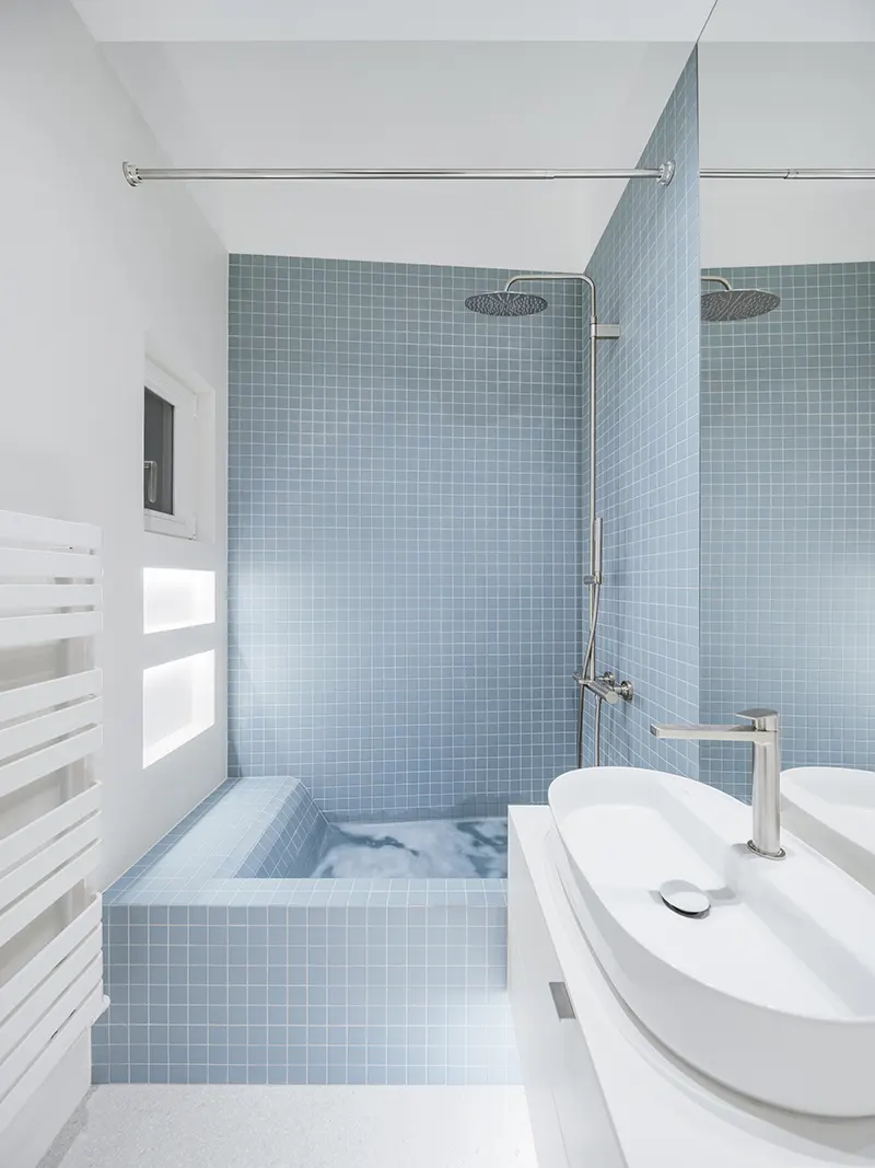 Il cubo verde che riorganizza lo spazio: dentro un piccolo appartamento a Praga 6 Bagno con mosaico blu polvere, vasca e doccia combinate in un unico volume