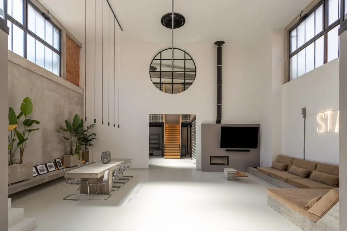 Casa brutalista in Versilia: soggiorno a doppia altezza con cemento a vista, camino e insegna al neon