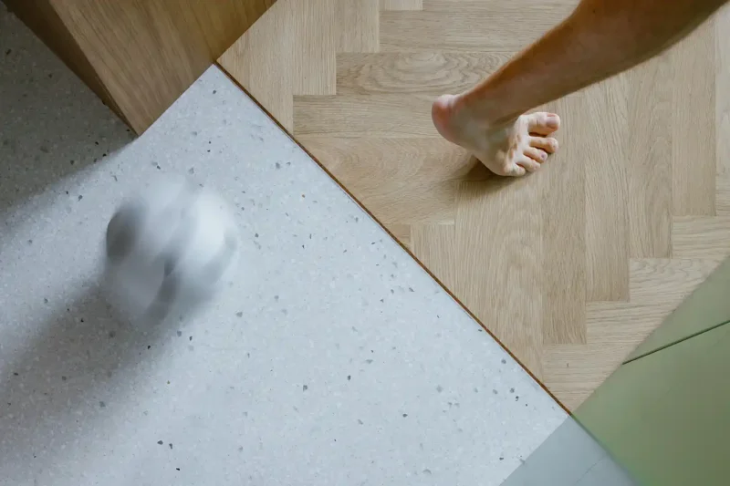 Il cubo verde che riorganizza lo spazio: dentro un piccolo appartamento a Praga 8 Dettaglio del passaggio tra parquet a spina di pesce e pavimento in terrazzo nel piccolo appartamento
