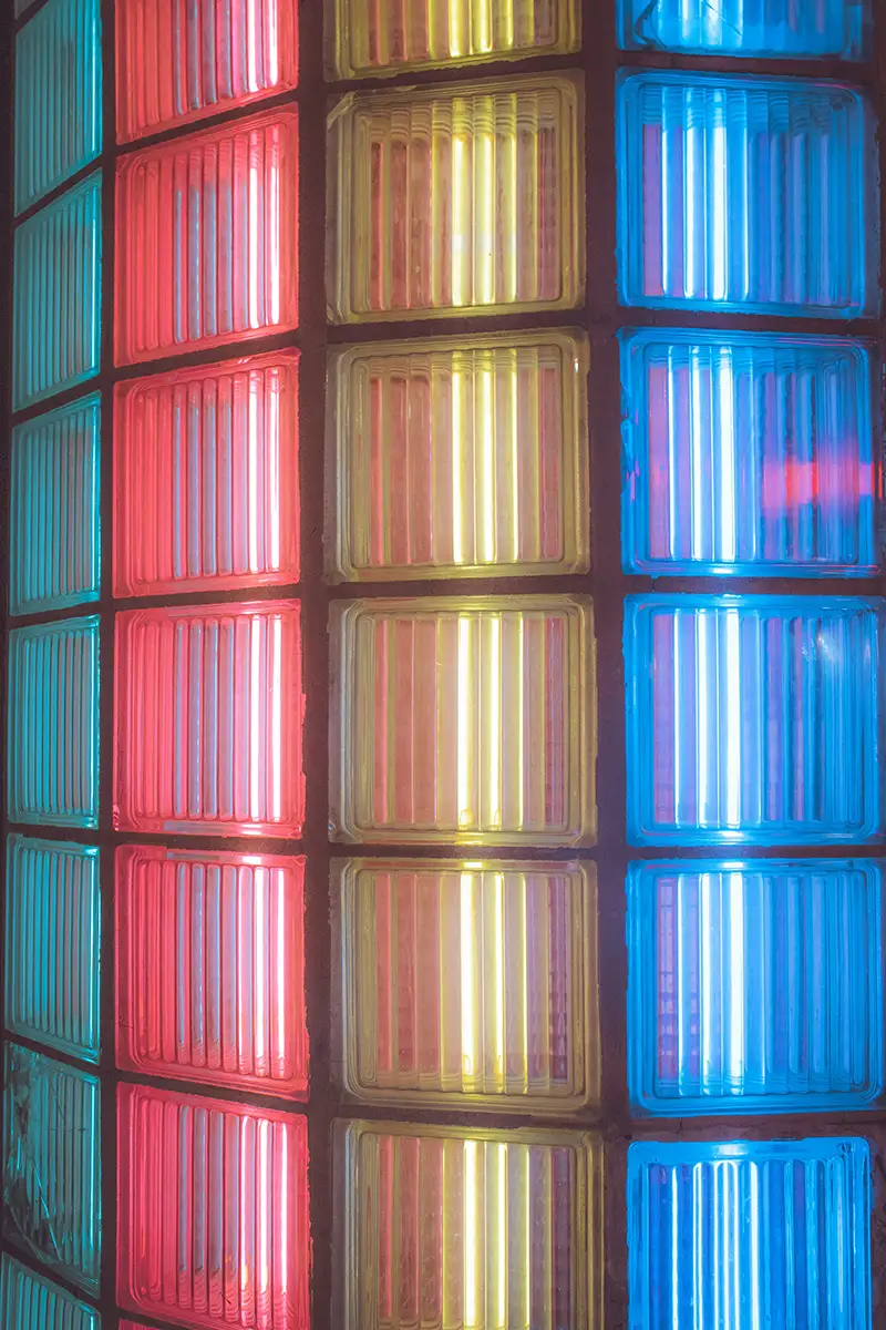 Dettaglio di vetrocemento colorato retroilluminato nei toni verde acqua, rosso, giallo e blu