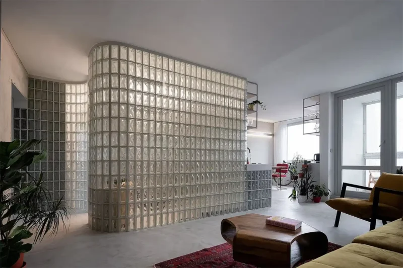 Ampia parete curva in vetrocemento moderno che separa cucina e soggiorno in un loft con arredi vintage e grandi vetrate