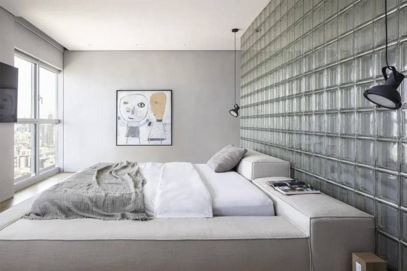 Parete in vetrocemento dietro il letto in una camera matrimoniale minimale grigia, per privacy e luce naturale